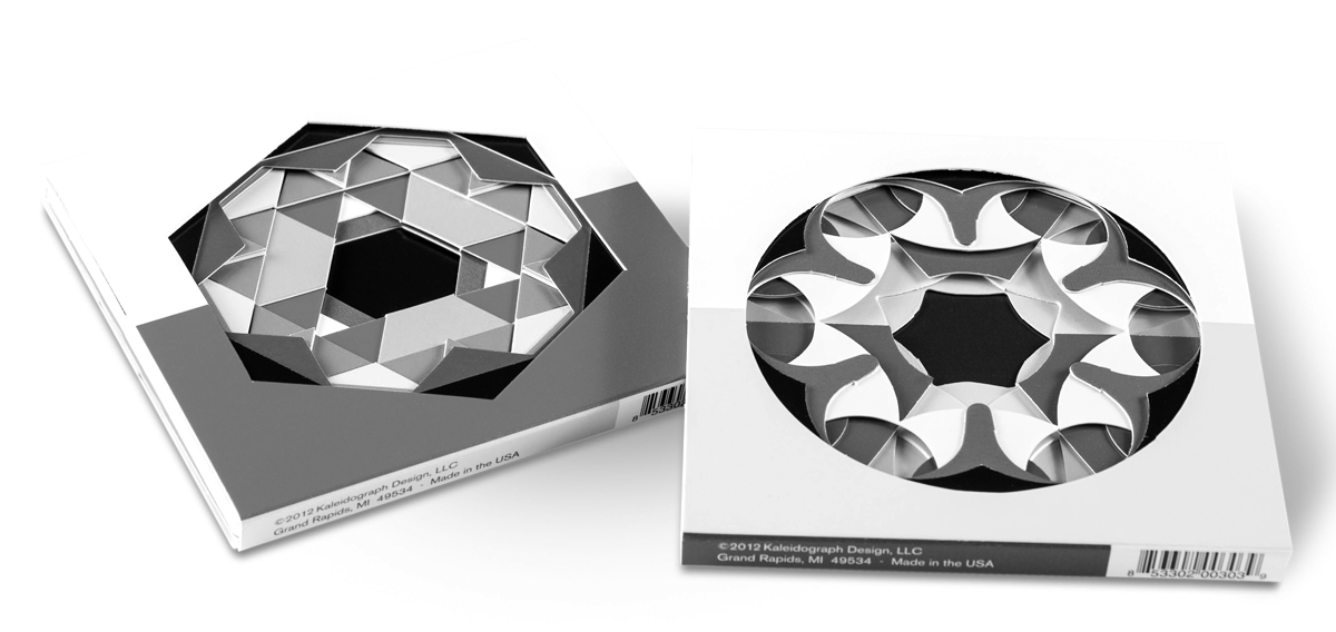 Two cardboard sleeves, each containing a stack of a dozen cards of varying colors, with different geomtric shapes cut out of each. The first sleeve displays the cards through a die-cut hexagon; the second sleeve’s corresponding die-cut is a circle.